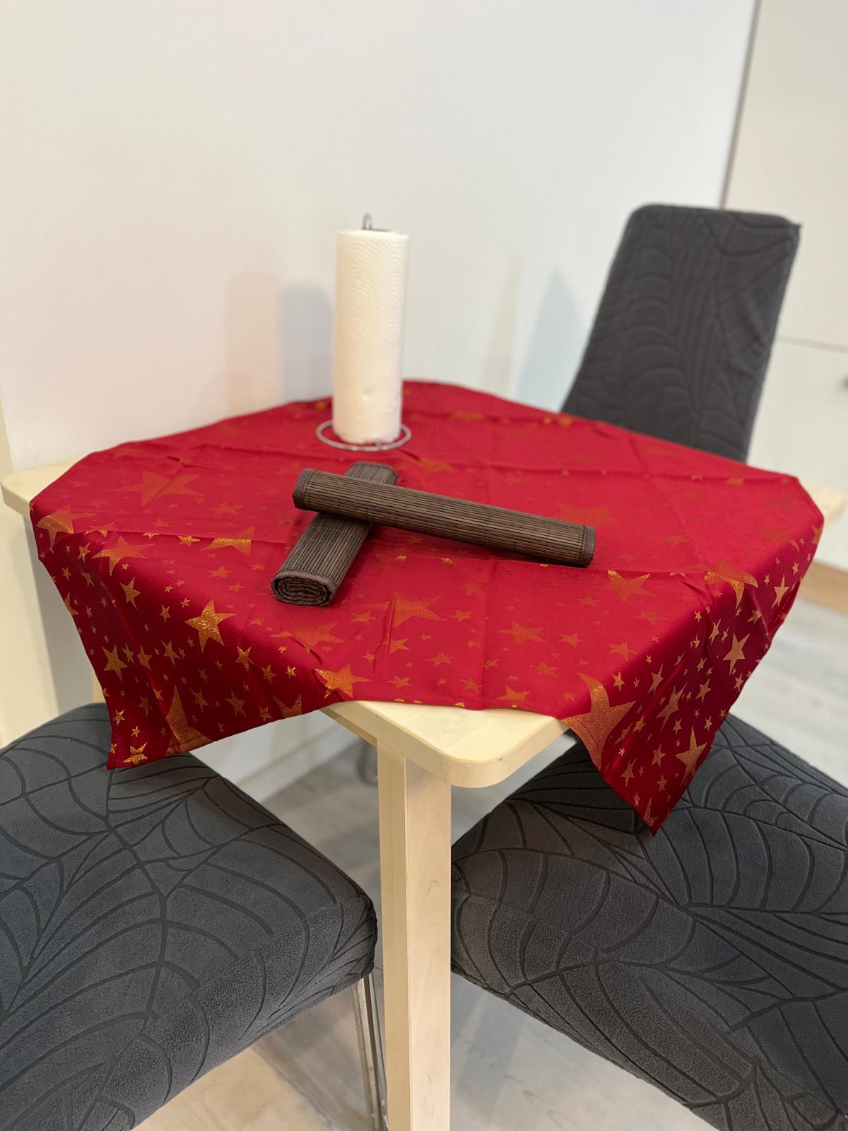 Runder Tisch mit rotem Tischdecken, Kerze und schwarzem Gegenstand auf zwei Stühlen.